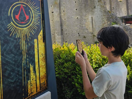 Un joueur scanne avec son téléphone l'affiche du Trésor Perdu d'Aliénor, posée au pied d'un monument