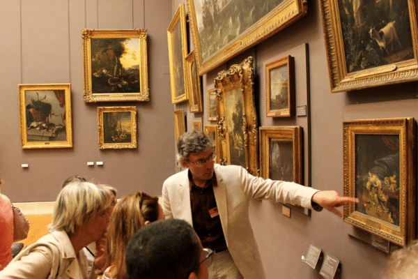 Photo d'une guide qui fait visiter le musée et présente une œuvre à un groupe de visiteurs.